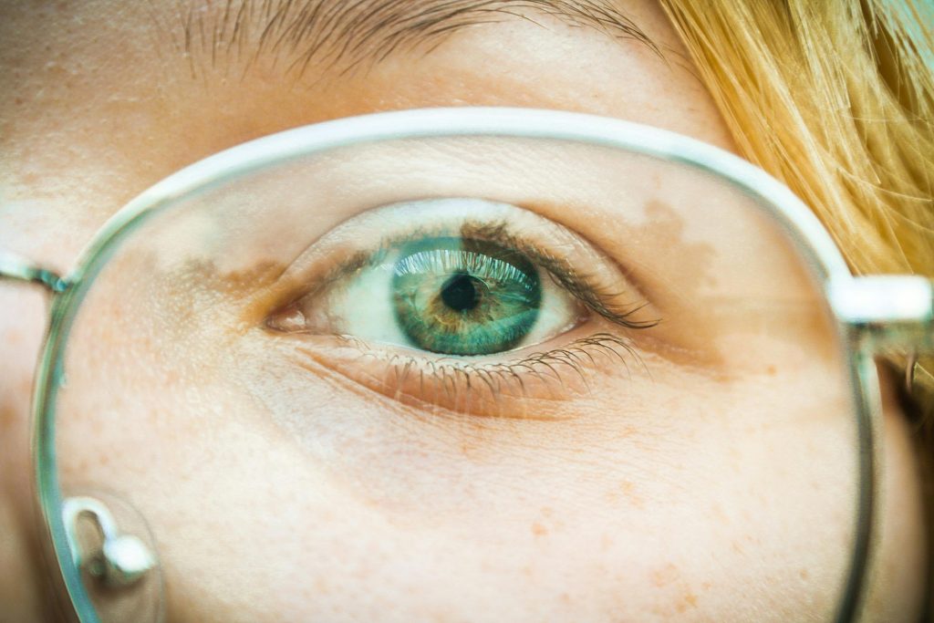Home Detailed close-up of a person wearing glasses, highlighting blue eyes and blonde hair.